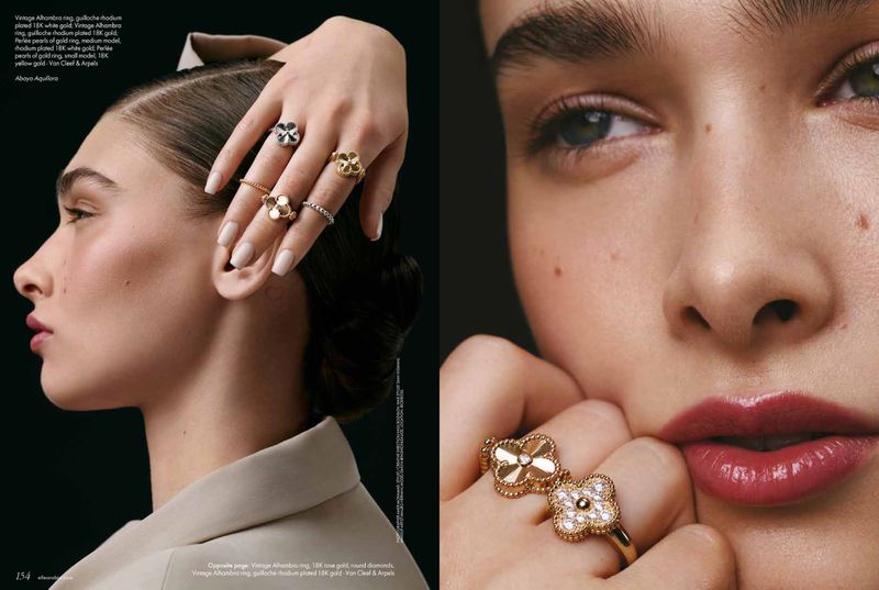 Close-up of a woman's face and hand with rings, featuring gold floral designs, against a dark background in a beauty editorial.