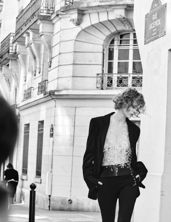 A woman poses in a black blazer and top in an urban fashion shoot. Black and white photography with architectural backdrop and street sign.