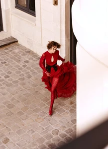 Model in red dress and red patterned tights walking across a cobblestone courtyard