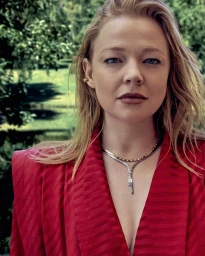 Portrait of actress Sarah Snook wearing a red blazer and layered necklaces against an outdoor park background