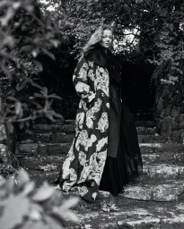 Sarah Snook wearing a patterned coat standing on a stone staircase in a wooded setting for Vogue Australia