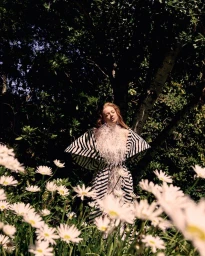 Sarah Snook wearing a black and white patterned dress in a garden surrounded by white daisies for Vogue Australia