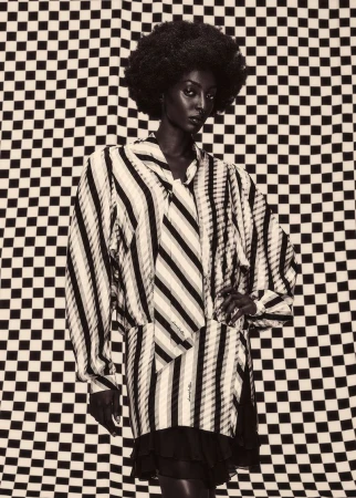 Black woman with an afro wearing a striped long-sleeve dress against a checkered backdrop in a monochrome fashion editorial portrait.