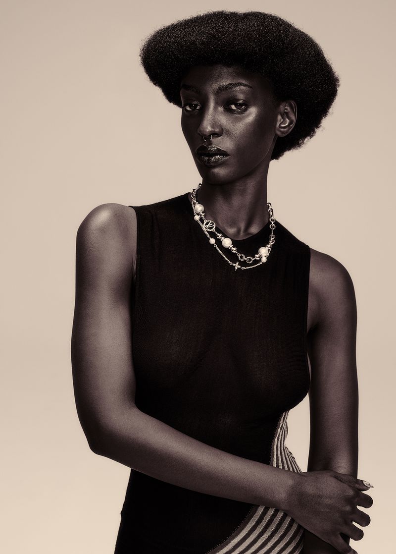 Portrait of a Black woman wearing a black sleeveless top and layered pearl necklace against a neutral background