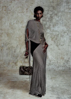 Black woman wearing a striped dress and holding a monogram handbag against a textured concrete wall