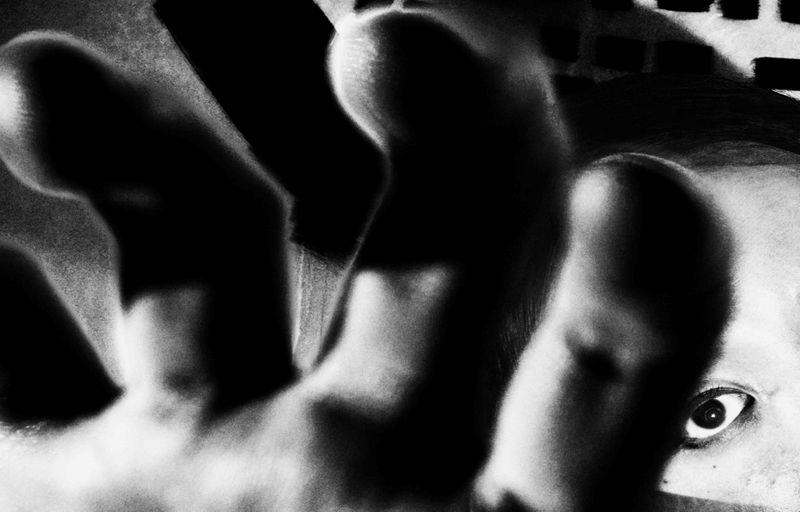 Monochrome image of an eye peering through fingers creates an abstract and stark, high-contrast composition, with a close-up, unusual perspective.