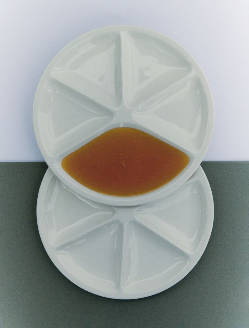 Overhead shot of stacked white sectioned plates, one partially filled with amber liquid against a split white and grey background.
