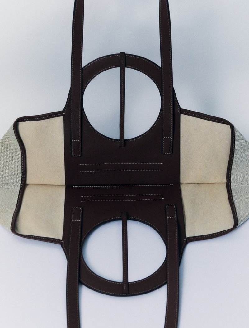 Overhead shot of an open brown and beige tote bag with round handles against a white background in a studio setting, product photography.