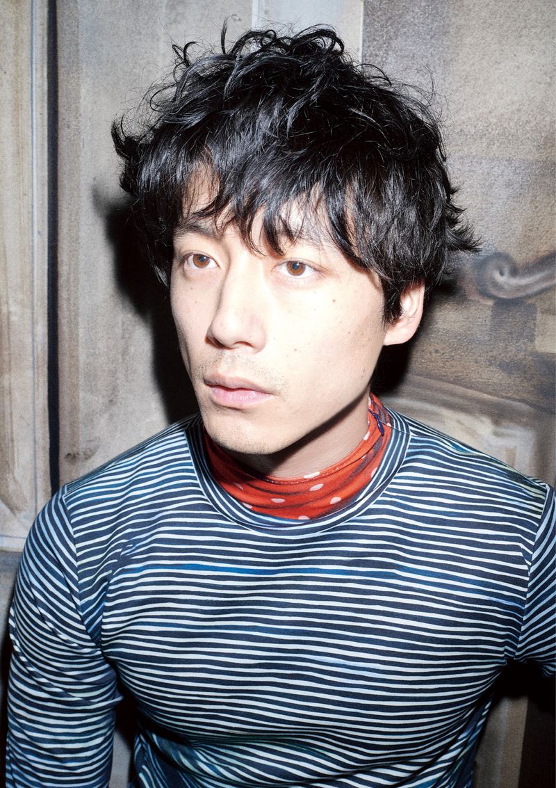 Portrait of an Asian man with dark, curly hair, wearing a blue and white striped shirt, posing in a soft, natural indoor setting.