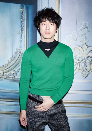 Japanese actor Kentaro Sakaguchi wearing a green sweater and patterned trousers against blue paneling.