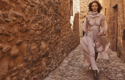 Model Birgit Kos walking down a narrow stone alleyway in a pale pink ruffled dress for Zimmermann Fall RTW