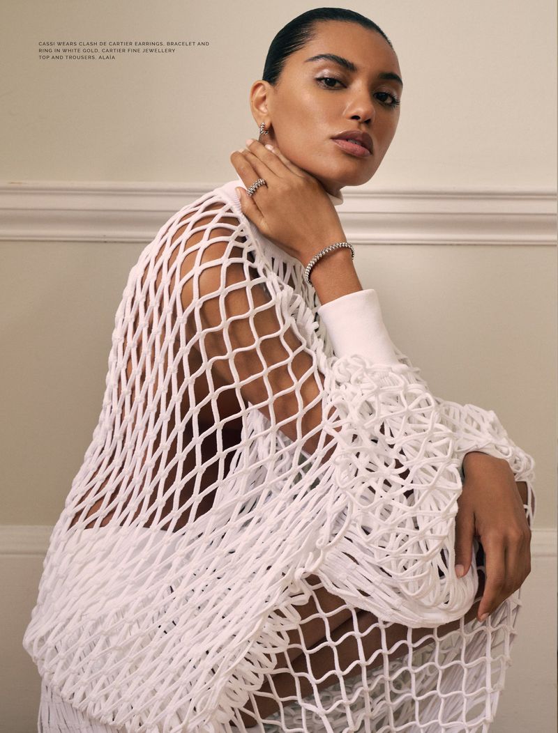 Elegant adult female poses indoors wearing a white netted top and jewellery, including earrings, a ring, and a bracelet.