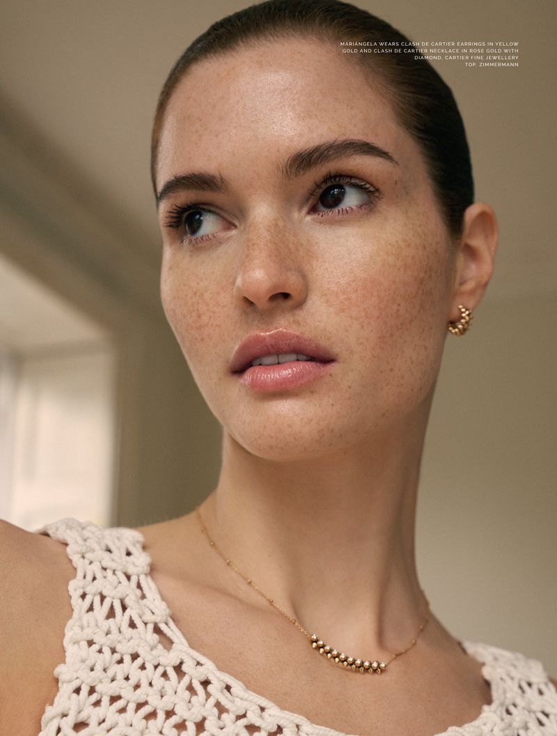Close-up portrait of a woman with freckles wearing hoop earrings and a white textured knit top against an out-of-focus background.