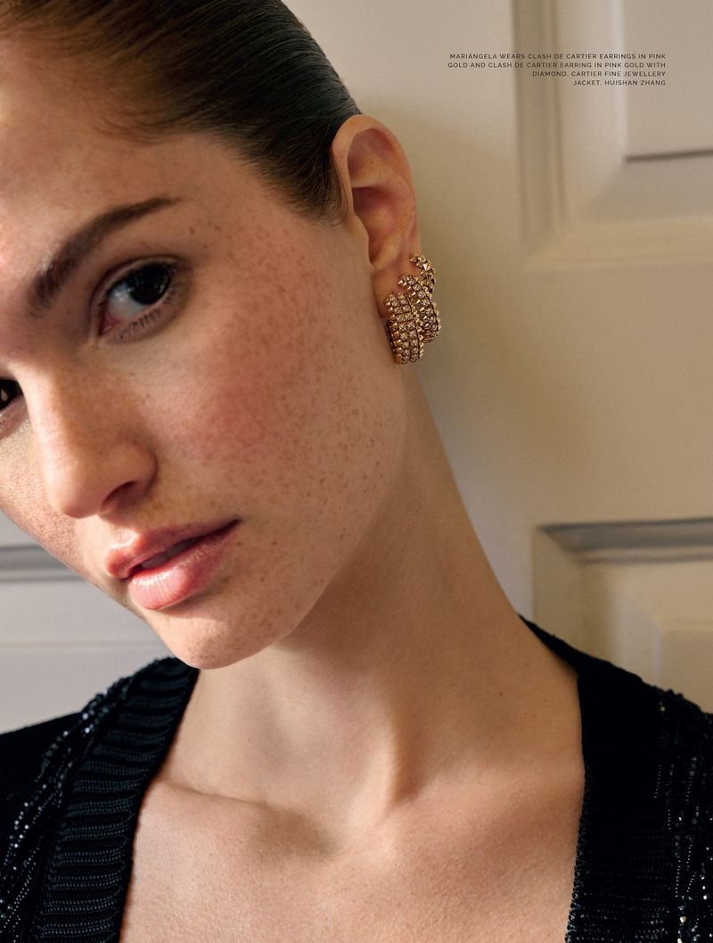 Close-up portrait of an adult woman wearing gold earrings and a black sequined jacket in front of a neutral interior wall.