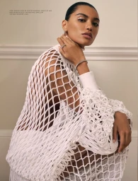 Model wearing white fishnet top touching diamond bracelet against a pale wall