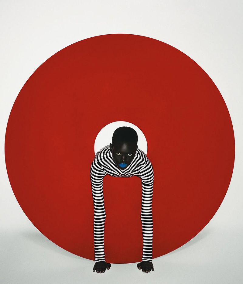 Striking studio portrait of an African-American woman with blue lips wearing a striped top posing behind a large red circle.
