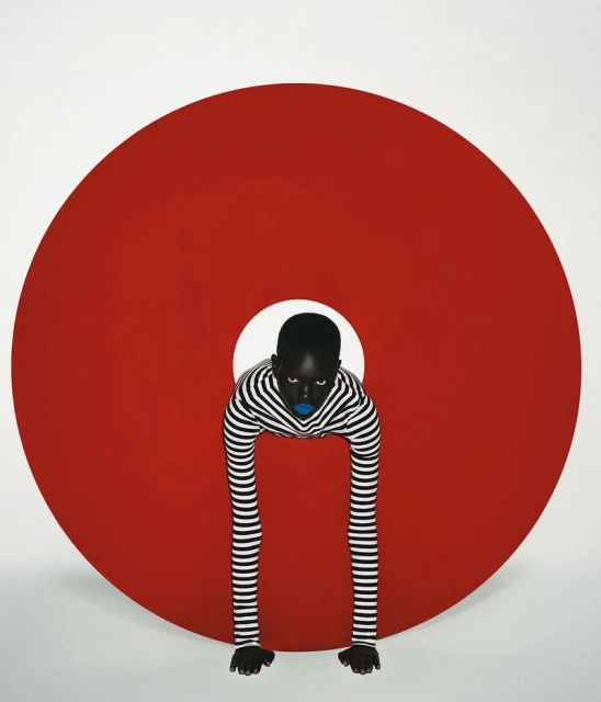 Striking studio portrait of an African-American woman with blue lips wearing a striped top posing behind a large red circle.