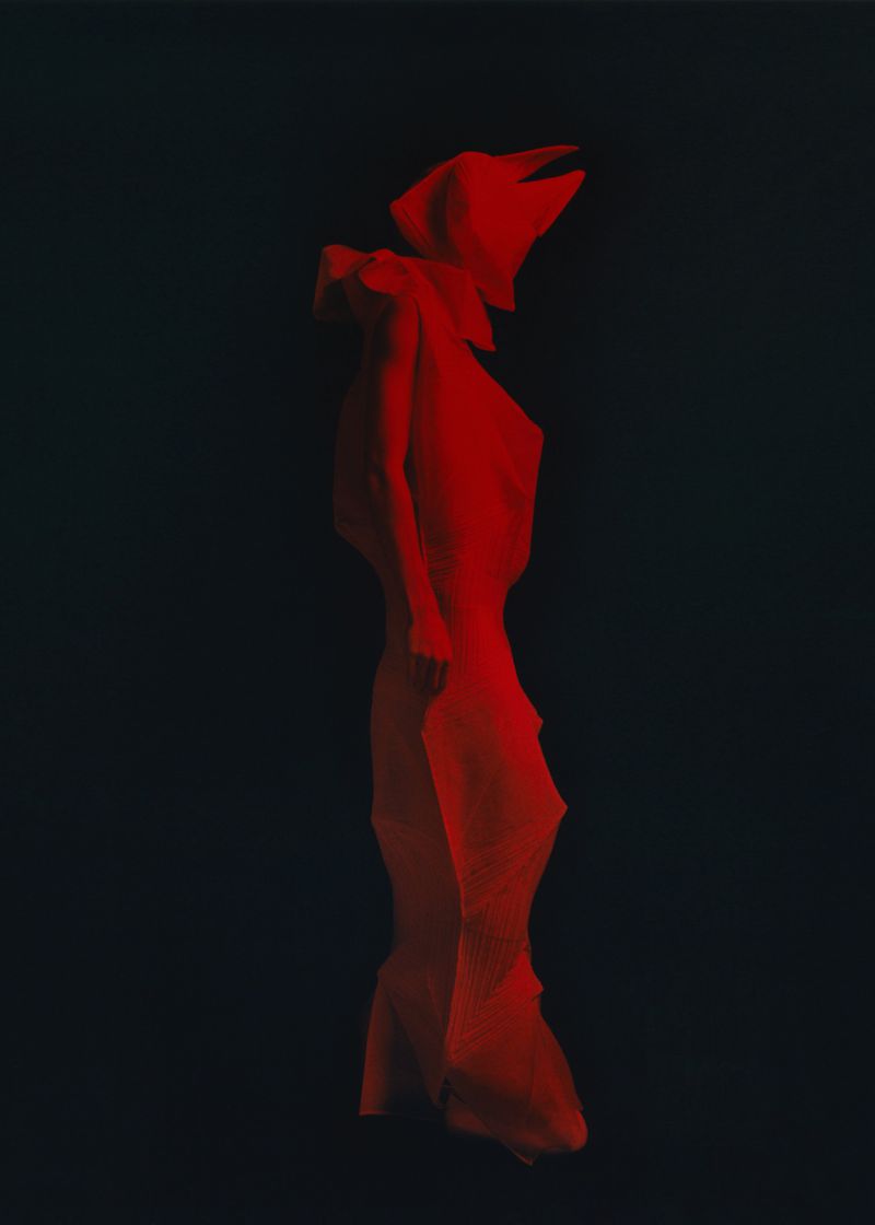 Abstract fashion image in red lighting: A model draped in flowing red fabric poses dramatically against a dark, gradient background.