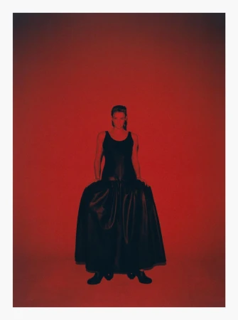 Model wearing a dark long dress standing against a vibrant red backdrop in a studio setting