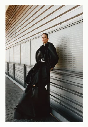 Model in a black sculptural dress leaning against a metallic industrial wall for Exhibition Magazine Ti Amo project