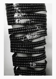 Close-up of legs wrapped in multiple black grommet belts against a plain background for Exhibition Magazine Ti Amo editorial.