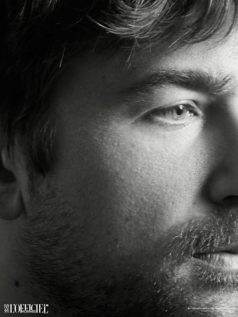 Monochromatic close-up portrait of a Caucasian adult male with stubble and dark hair, gazing slightly up, lit by studio lighting.
