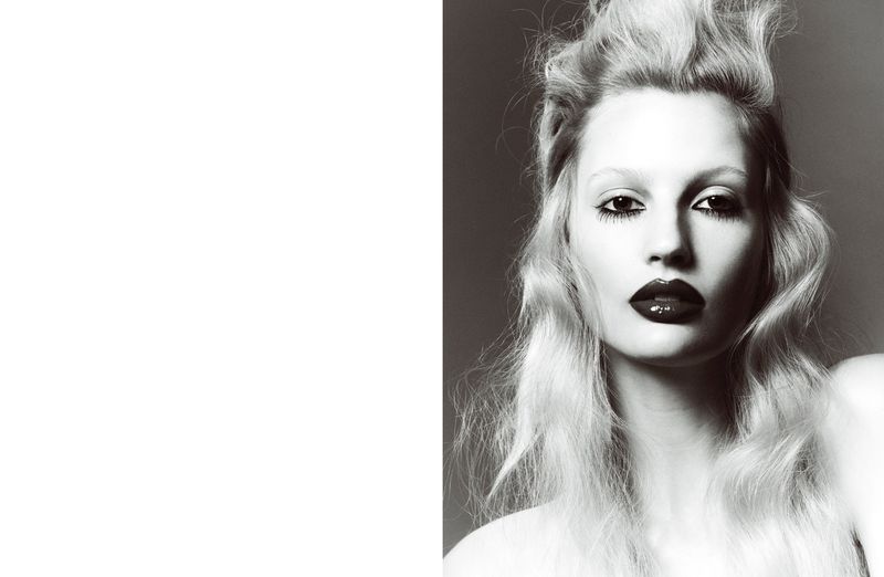Monochrome portrait of an adult woman with bleached blond hair, dark lipstick, and dramatic eye makeup, captured in a studio setting.