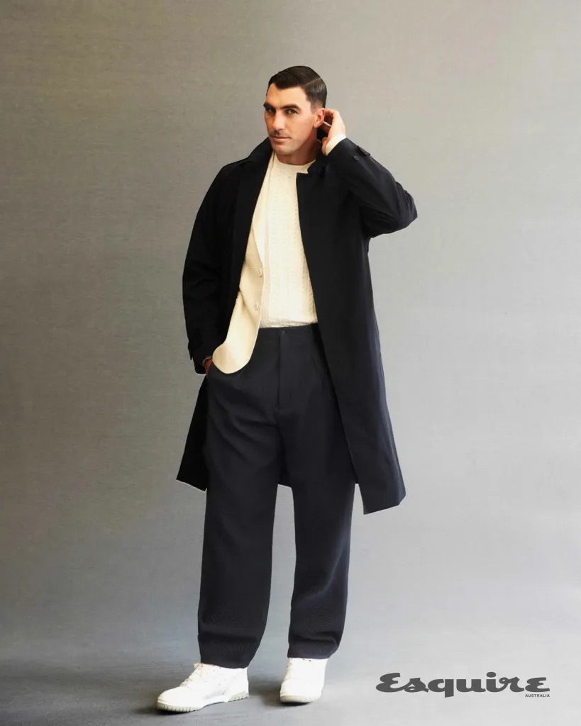 Man wearing a dark coat and trousers over a white shirt against a neutral grey studio background for Esquire Australia editorial.