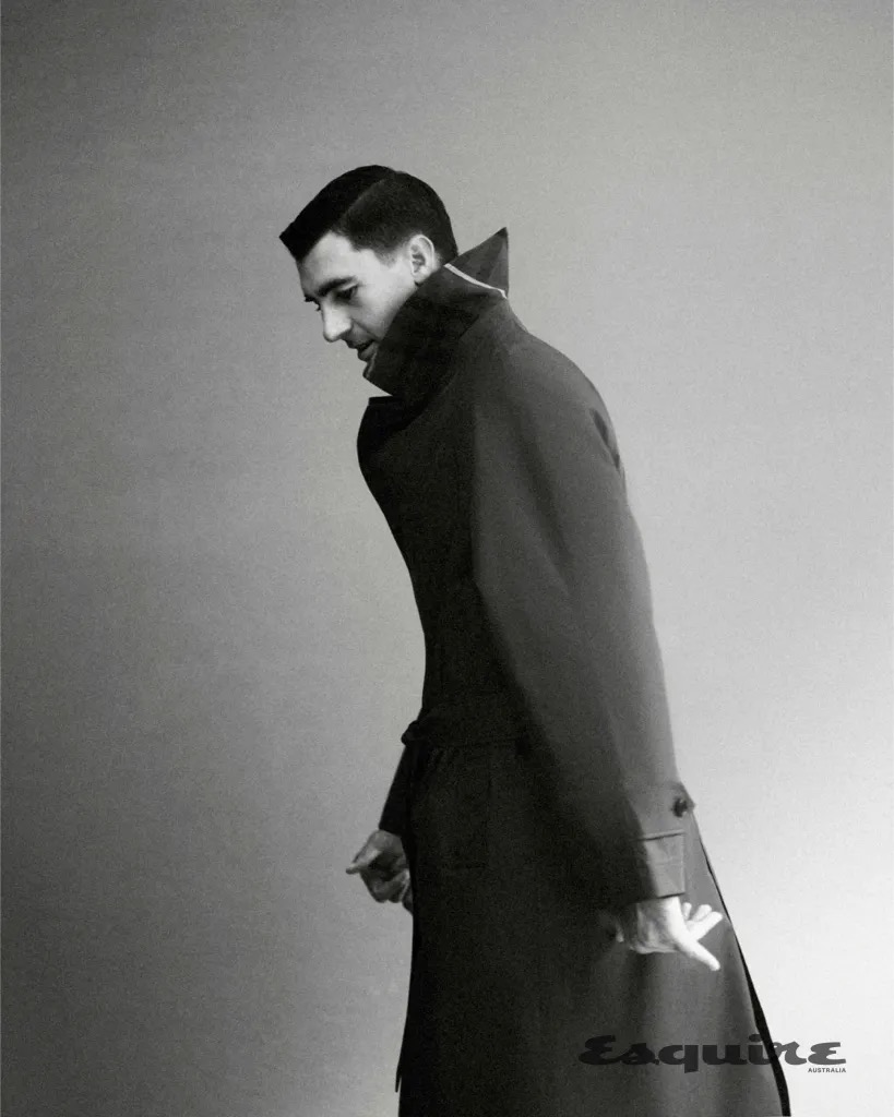 Man wearing a dark trench coat against a plain studio background for an editorial portrait for Esquire Australia.