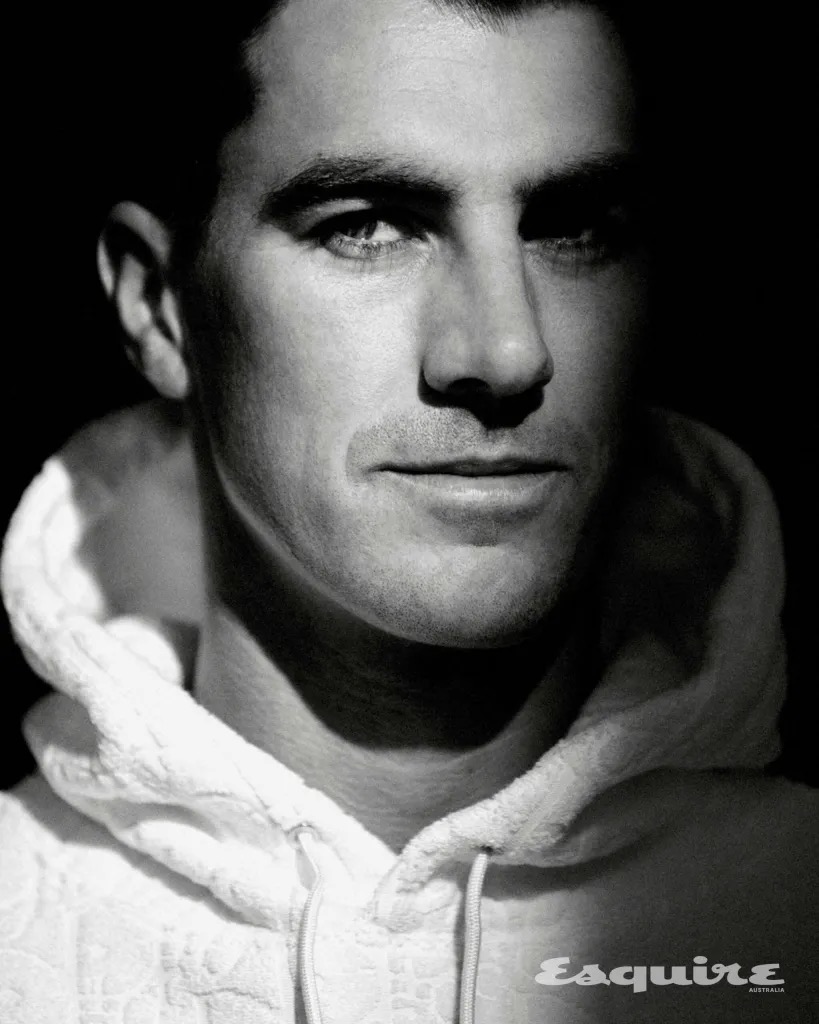 Black and white headshot of a man wearing a white hoodie, illuminated by studio lighting. The 'Esquire' logo is visible in the corner.