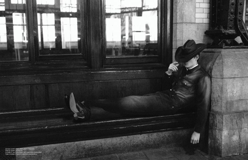 Black and white fashion shot of a man in a cowboy hat and denim suit reclining against a building, showcasing editorial style.