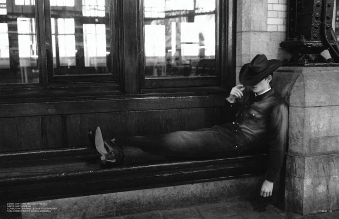 Black and white fashion shot of a man in a cowboy hat and denim suit reclining against a building, showcasing editorial style.
