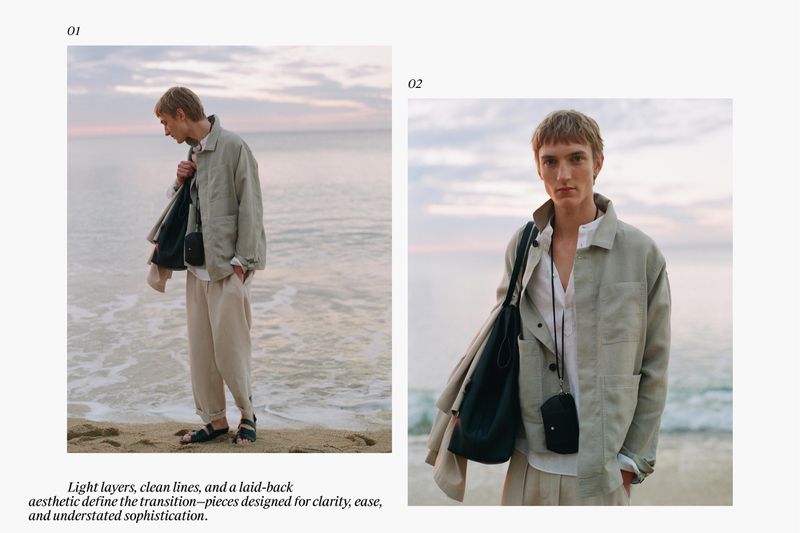 Model wearing a light jacket and loose trousers holding a dark tote bag on a sandy beach