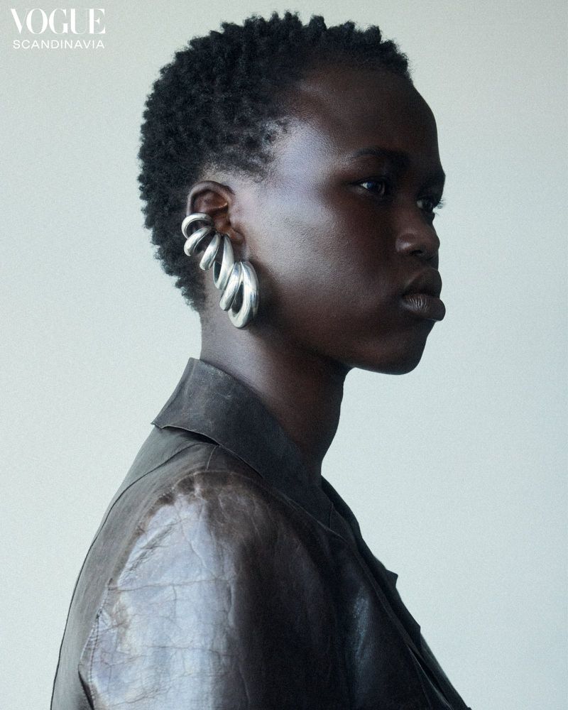 Portrait of an African-descent adult female model wearing a leather jacket and large silver earrings against a neutral backdrop.
