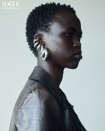 Portrait of an African-descent adult female model wearing a leather jacket and large silver earrings against a neutral backdrop.