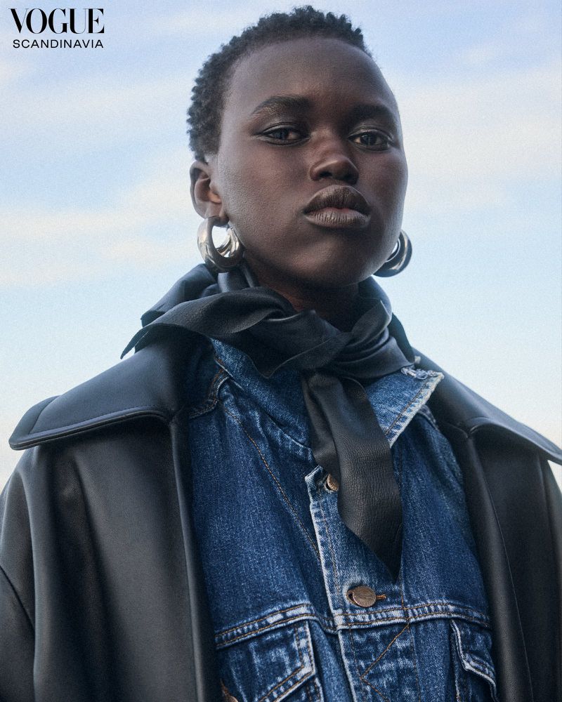 Portrait of a Black woman wearing a denim jacket, hoop earrings, and a black scarf against a blue sky, Vogue Scandinavia logo visible.