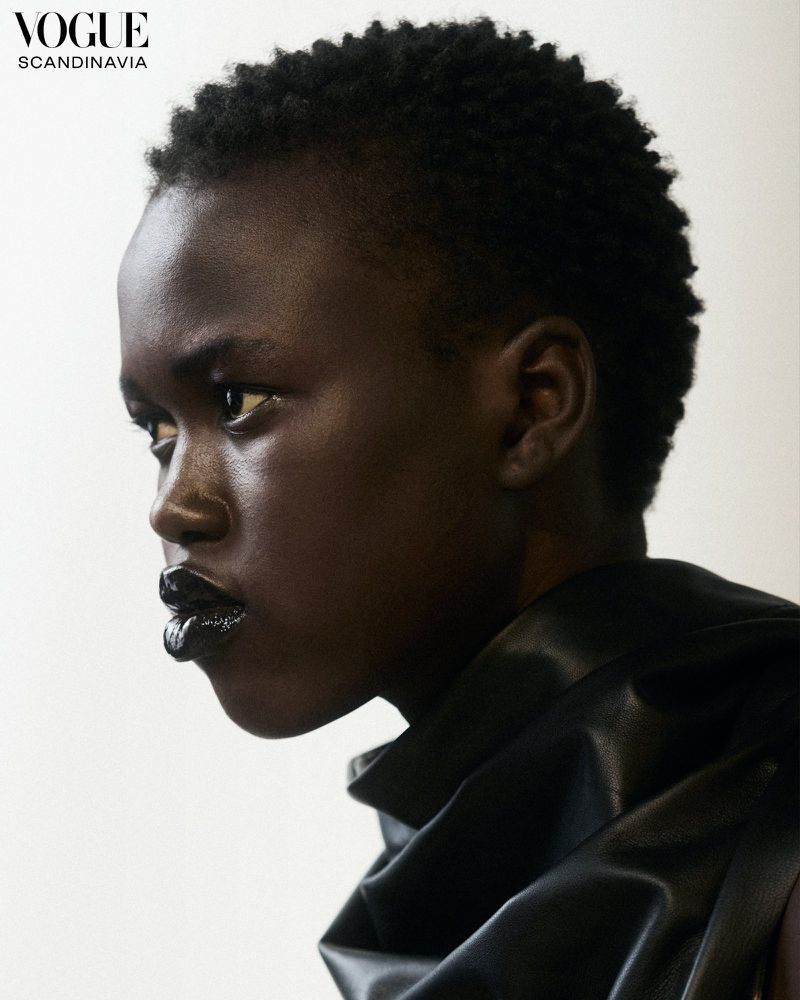 Close-up portrait of a dark-skinned woman with short hair and dark lipstick, wearing a black top, shot in a photo studio.