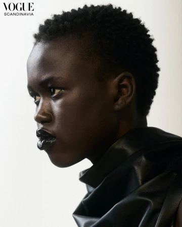 Close-up portrait of a dark-skinned woman with short hair and dark lipstick, wearing a black top, shot in a photo studio.