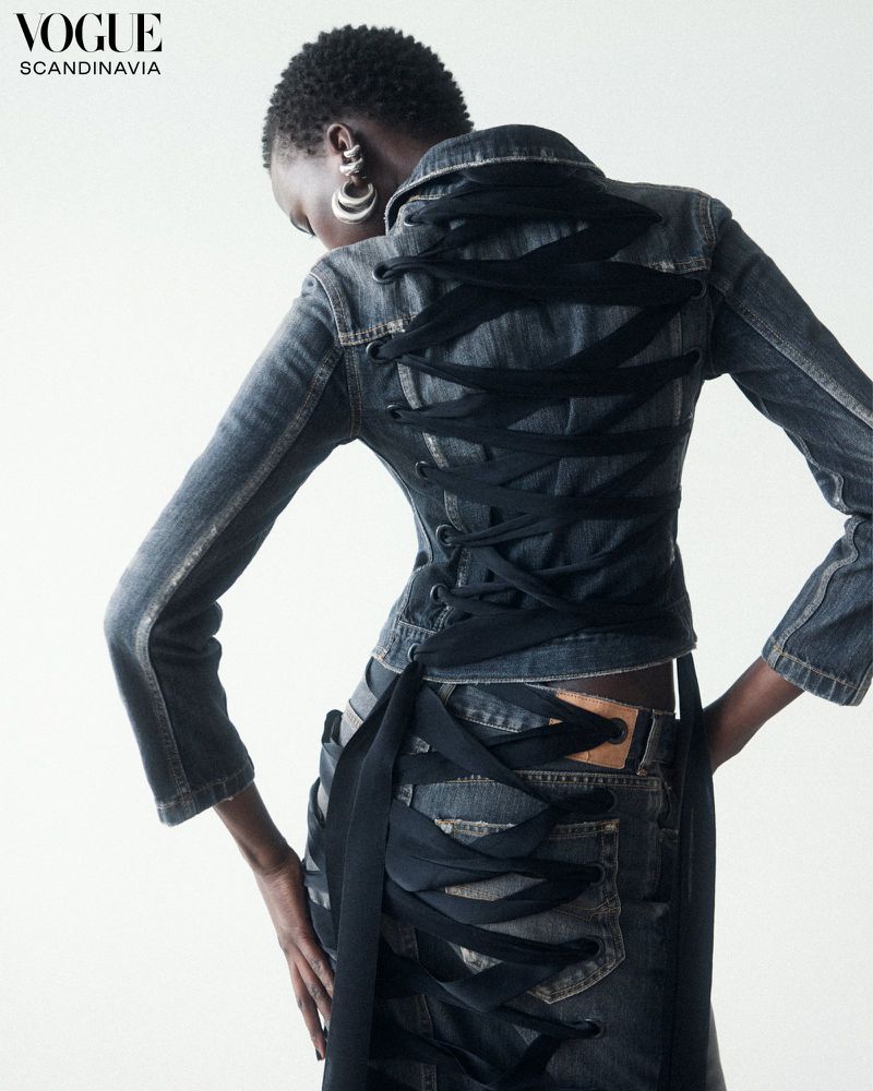 An African woman models denim jacket and skirt with black ribbon lacing up the back, shot in a bright studio for Vogue Scandinavia.