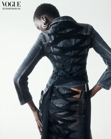 An African woman models denim jacket and skirt with black ribbon lacing up the back, shot in a bright studio for Vogue Scandinavia.