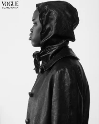 Profile portrait of a black woman wearing a black leather hooded coat against a plain white background