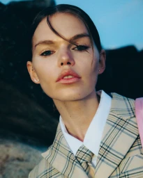 Close-up portrait of a female model wearing a plaid blazer and matching tie outdoors