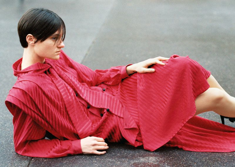 Woman in a red dress lies on a concrete surface. The female model has short dark hair and is wearing an elegant striped red dress.