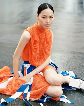 Model Jiahui Zhang wearing an orange textured top and blue-and-white patterned skirt sitting on pavement