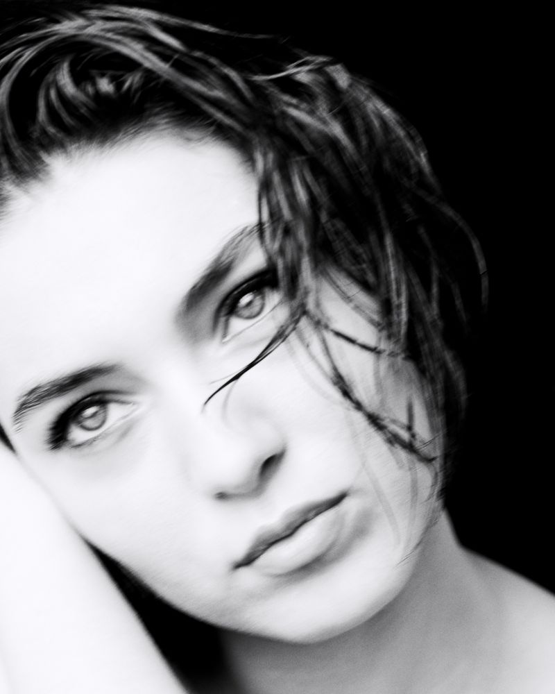 Monochrome portrait of a young woman with short, dark, wet hair, gazing intently at the camera against a dark background.