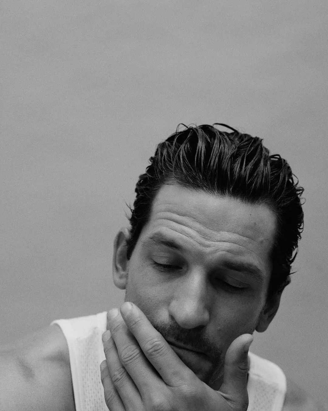 Monochrome portrait of a man with wet styled hair touching his chin against a plain grey background