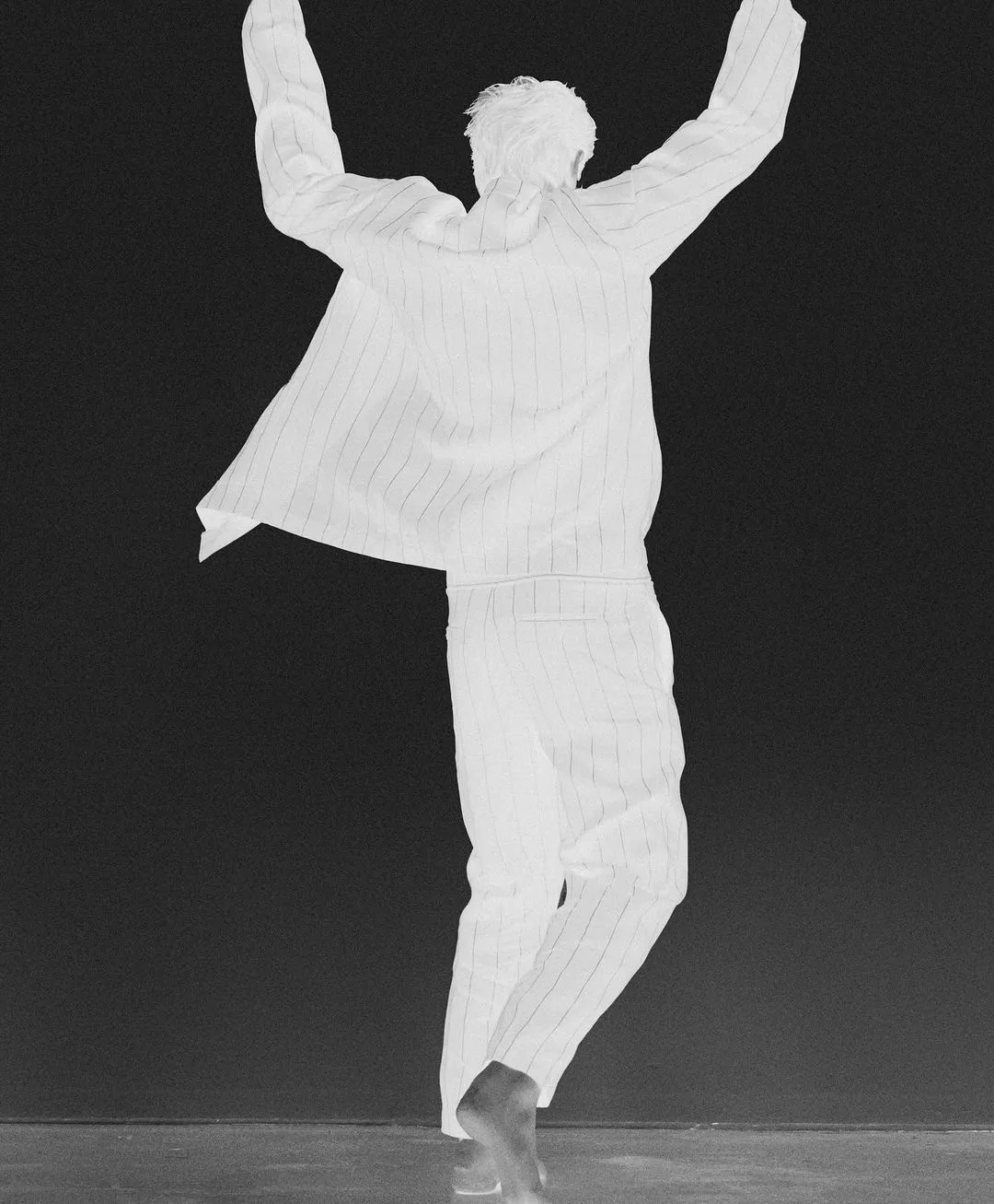 Negative image of a person jumping with arms raised wearing pinstripe trousers against a dark background