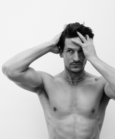Black and white portrait of a shirtless man with dark hair running his hands through his hair against a plain white background.