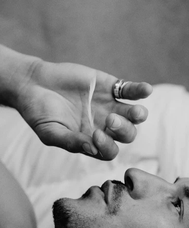 Close-up black and white portrait of a man lying down with a delicate feather hovering above his face.