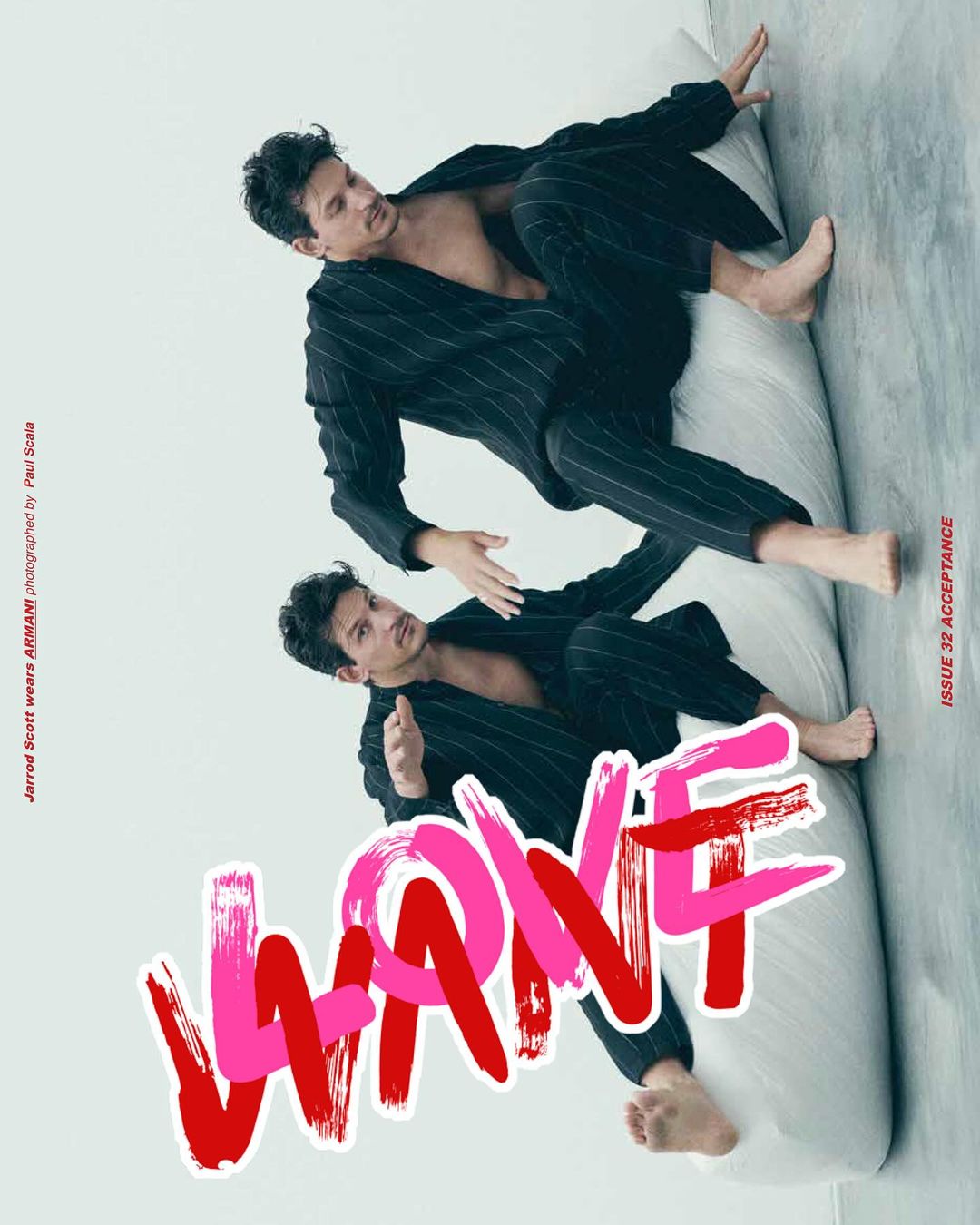 Two young adult males in pinstripe suits lounge on a mattress in a bright photo studio. Magazine cover featuring bold pink and red text.